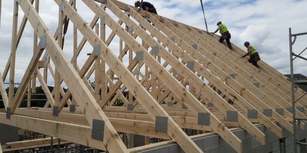 Wooden roof trusses installed on gable roof construction site showing triangular framework and metal connector plates